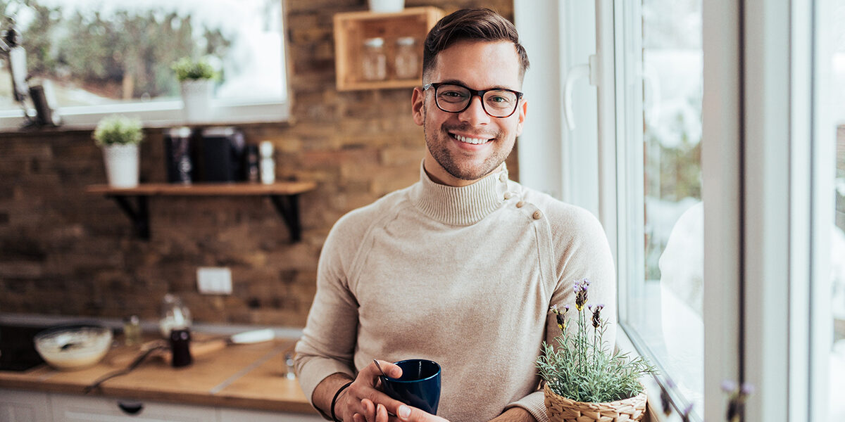 Portrait of smiling millenial man drinking tea near the window a