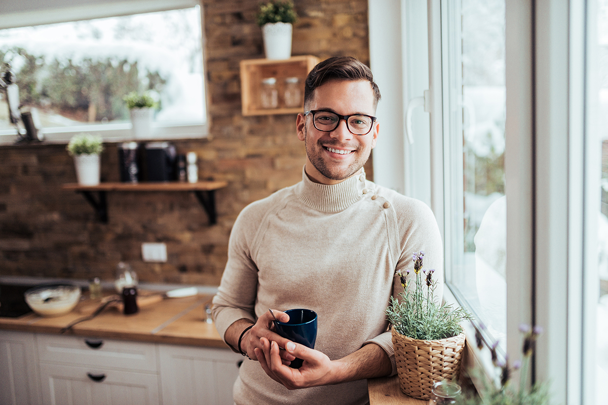 Portrait of smiling millenial man drinking tea near the window a