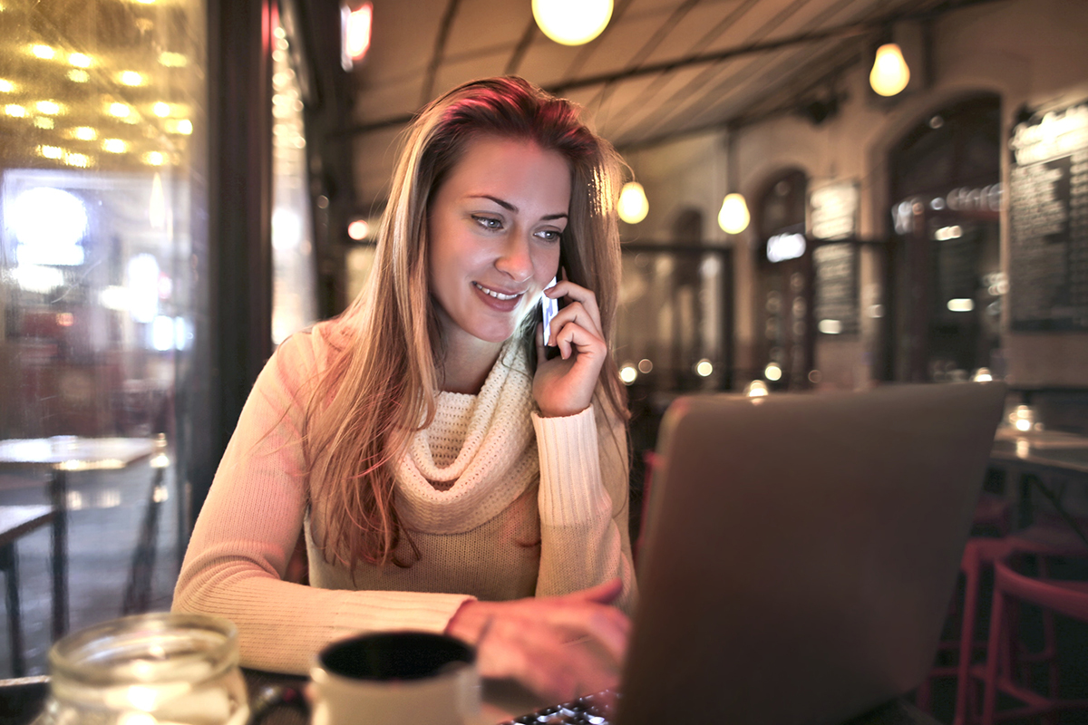30062020-relaxed-woman-in-cafe-talking-on-smartphone-and-using-laptop-3783522